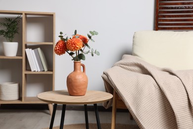 Ceramic vase with beautiful flowers on coffee table near armchair indoors