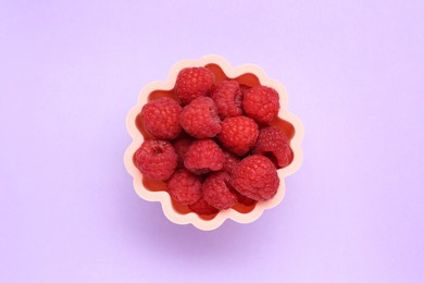 Photo of Bowl of fresh delicious raspberries on violet background, top view