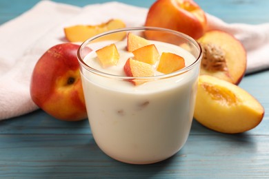Tasty peach yogurt with pieces of fruit in glass on light blue wooden table