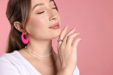 Photo of Young woman with lip and ear piercings on pink background, closeup. Space for text