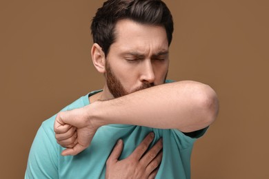 Photo of Sick man coughing into his elbow on brown background. Cold symptoms