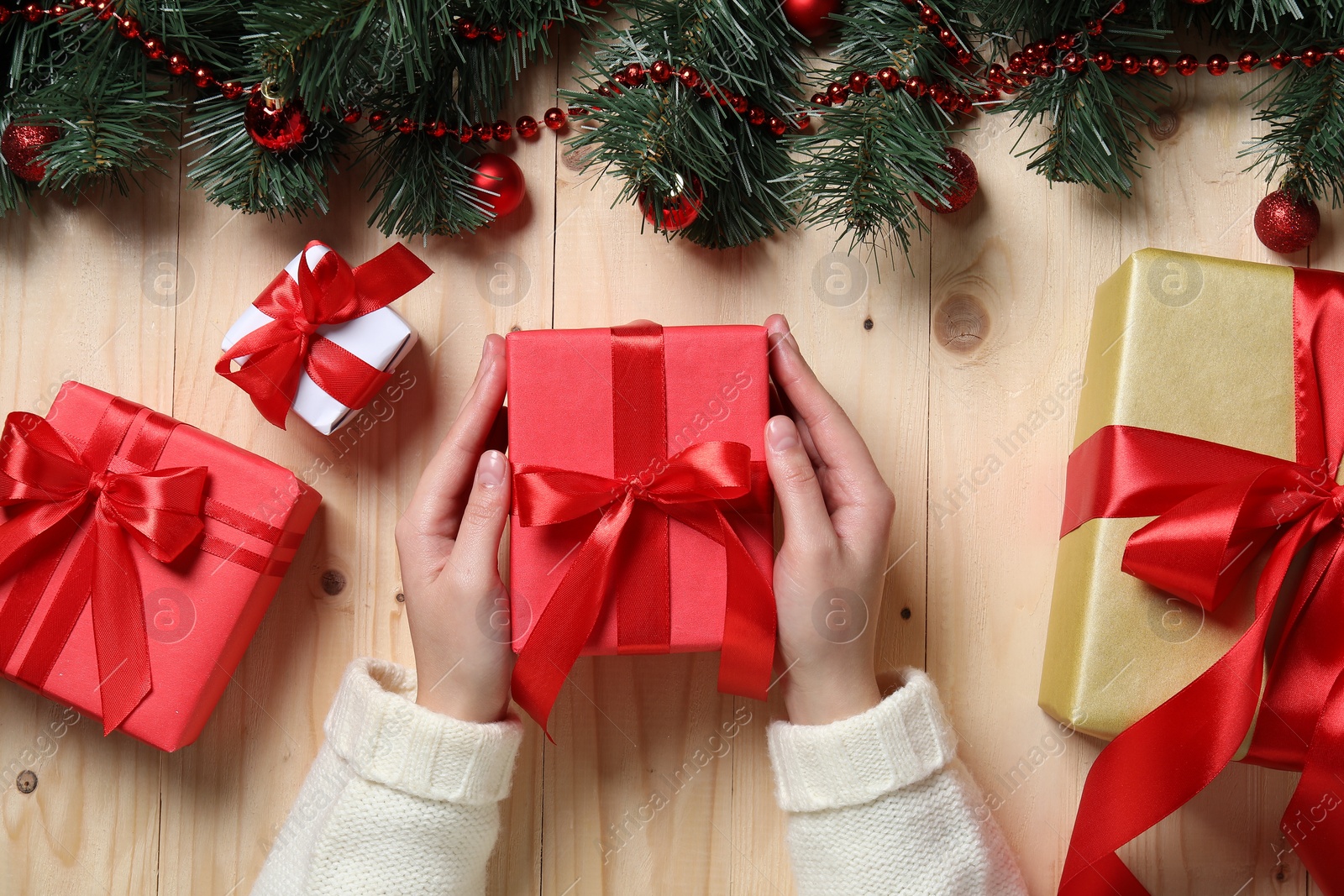 Photo of Christmas present. Woman with gift boxes and decorated fir tree branches at wooden table, top view