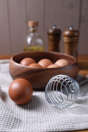 Photo of Making dough. Metal whisk and eggs in wooden bowl on table, closeup