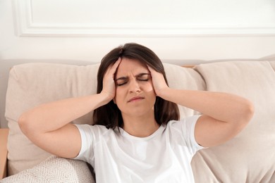 Photo of Young woman suffering from migraine on sofa at home