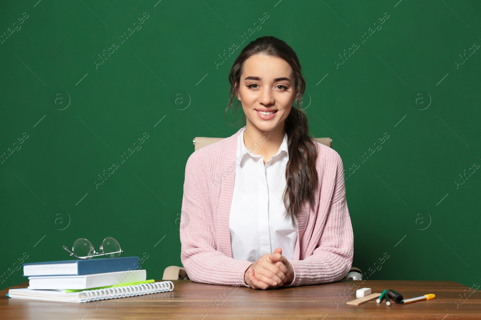 Photo of Portrait of beautiful young teacher sitting at table near chalkboard