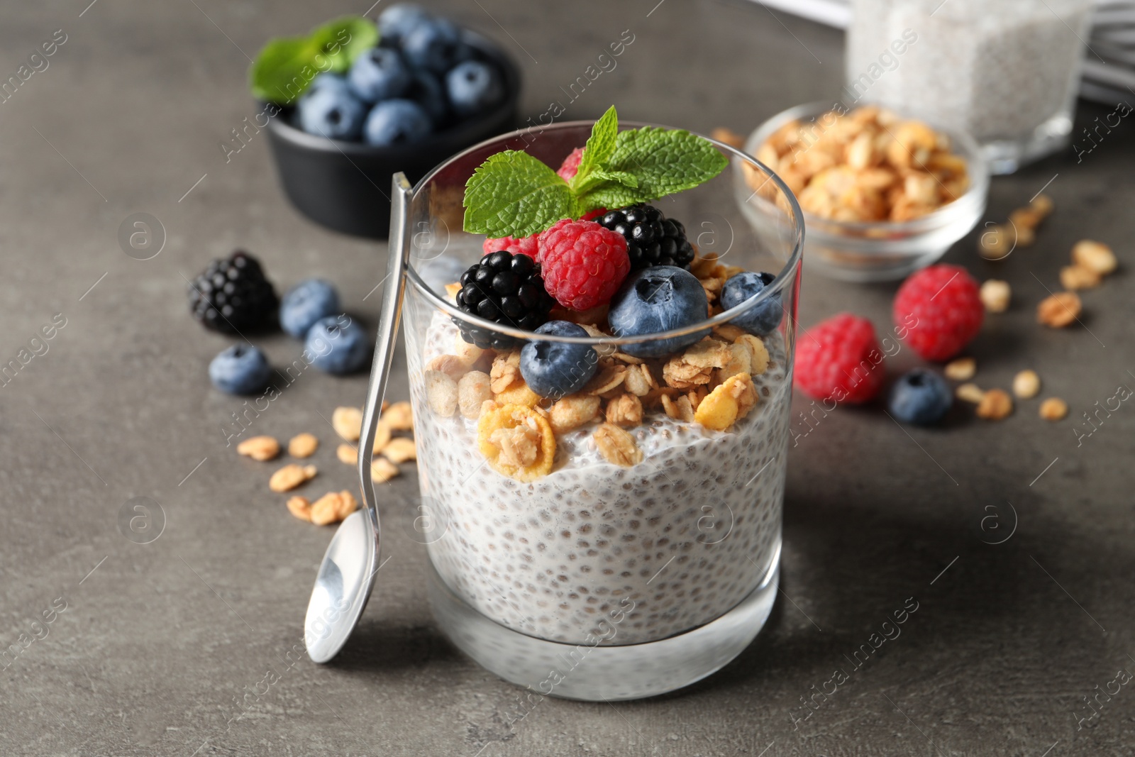 Photo of Delicious chia pudding with berries, granola and mint on grey table