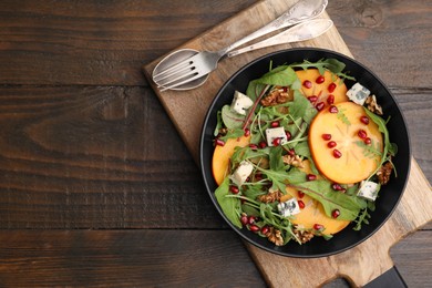 Photo of Tasty salad with persimmon, blue cheese, pomegranate and walnuts served on wooden table, top view. Space for text