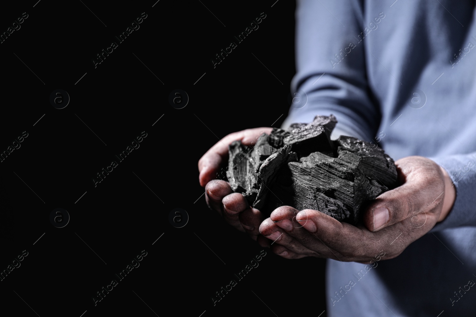 Photo of Man with handful of coal on dark background, closeup. Space for text