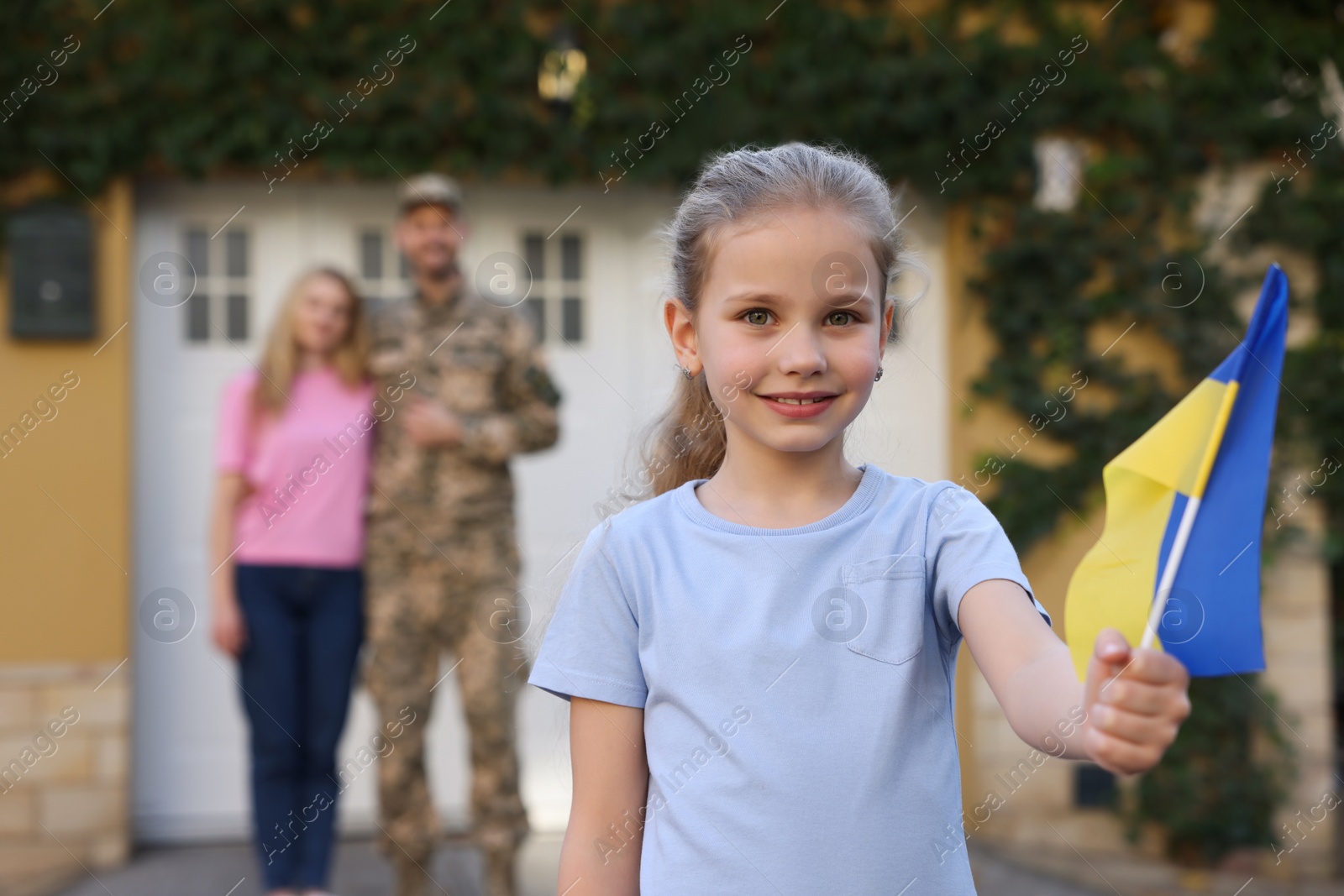 Photo of Child with Ukrainian flag, her father in military uniform and mother outdoors, space for text. Family reunion