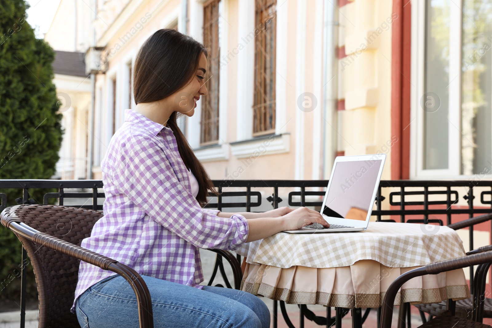 Image of Young woman working on laptop at outdoor cafe