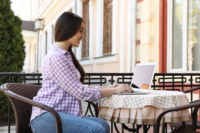 Image of Young woman working on laptop at outdoor cafe