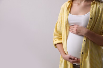 Photo of Pregnant woman on light grey background, closeup. Space for text