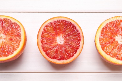 Photo of Halves of ripe red oranges on white wooden table, flat lay