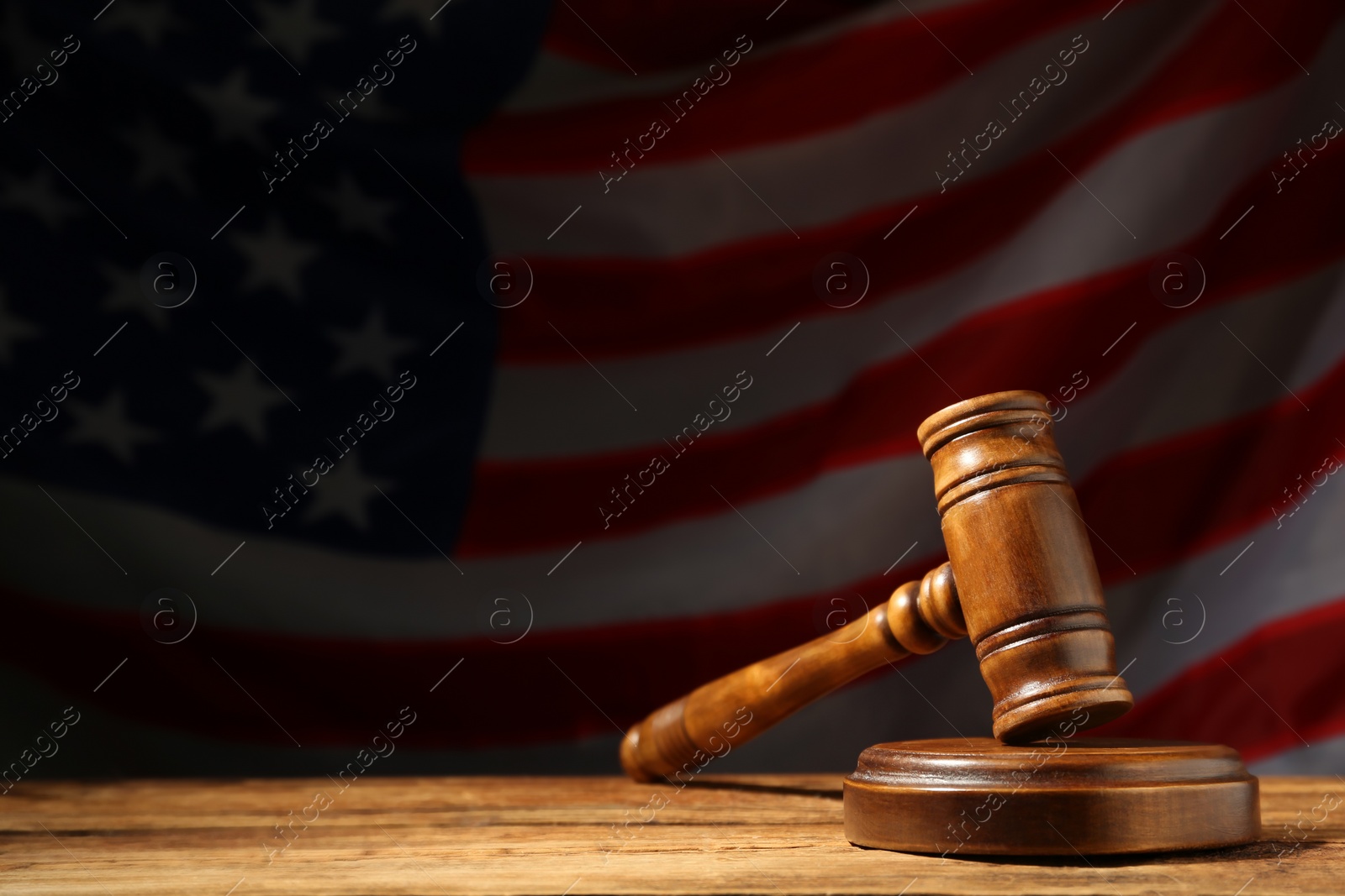 Photo of Judge's gavel on wooden table against American flag in darkness, space for text