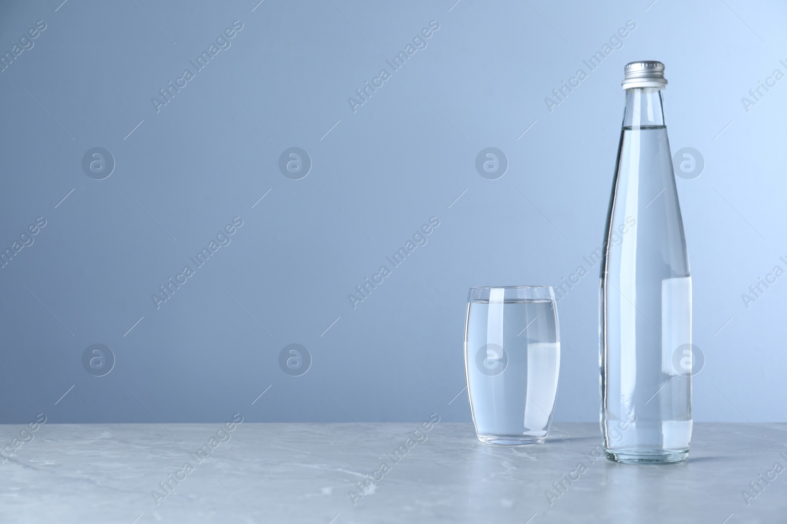 Photo of Glass and bottle with water on table against light blue background, space for text