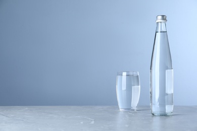 Photo of Glass and bottle with water on table against light blue background, space for text