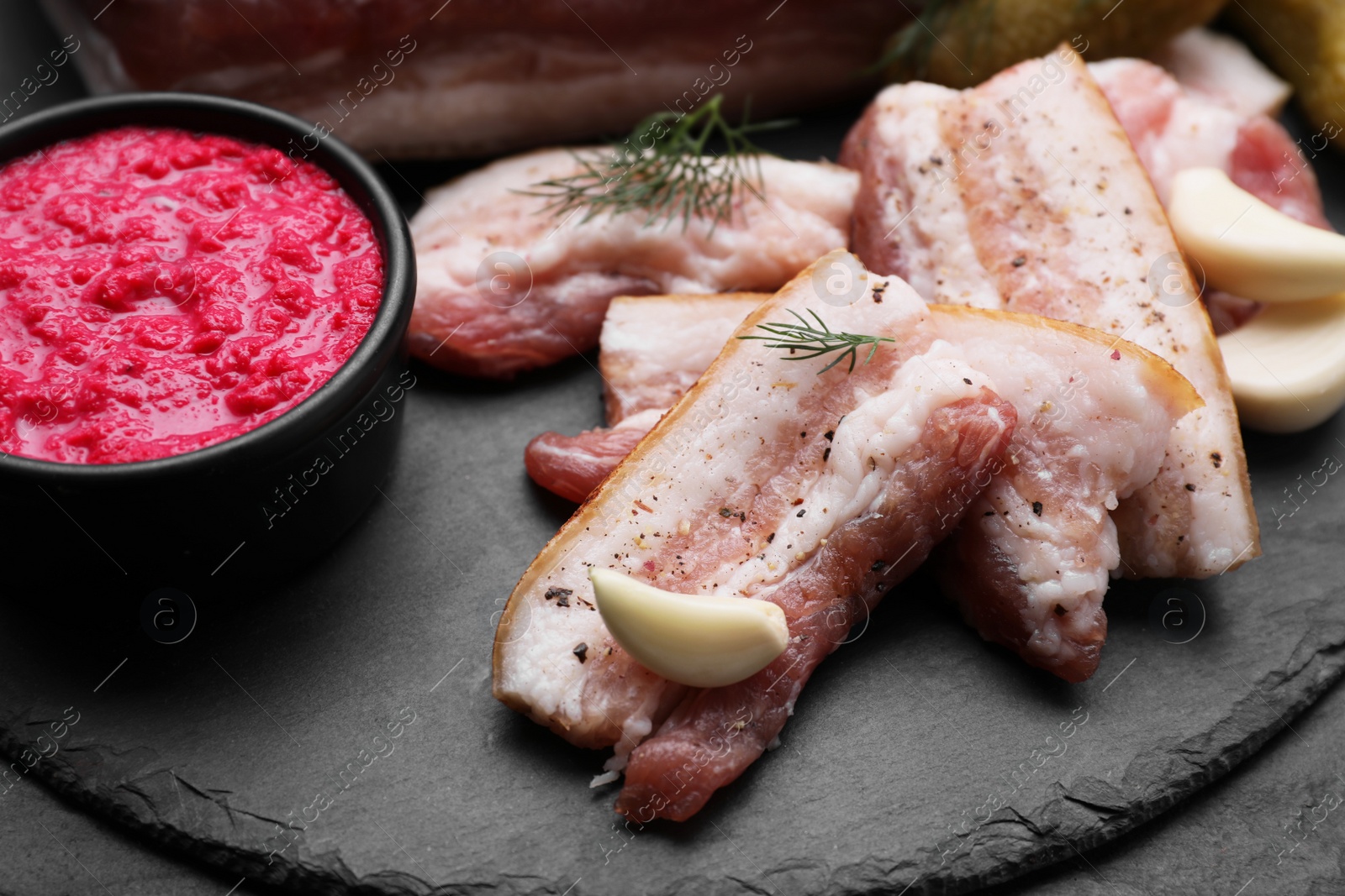 Photo of Tasty pork fatback with spices, garlic and sauce on black table, closeup