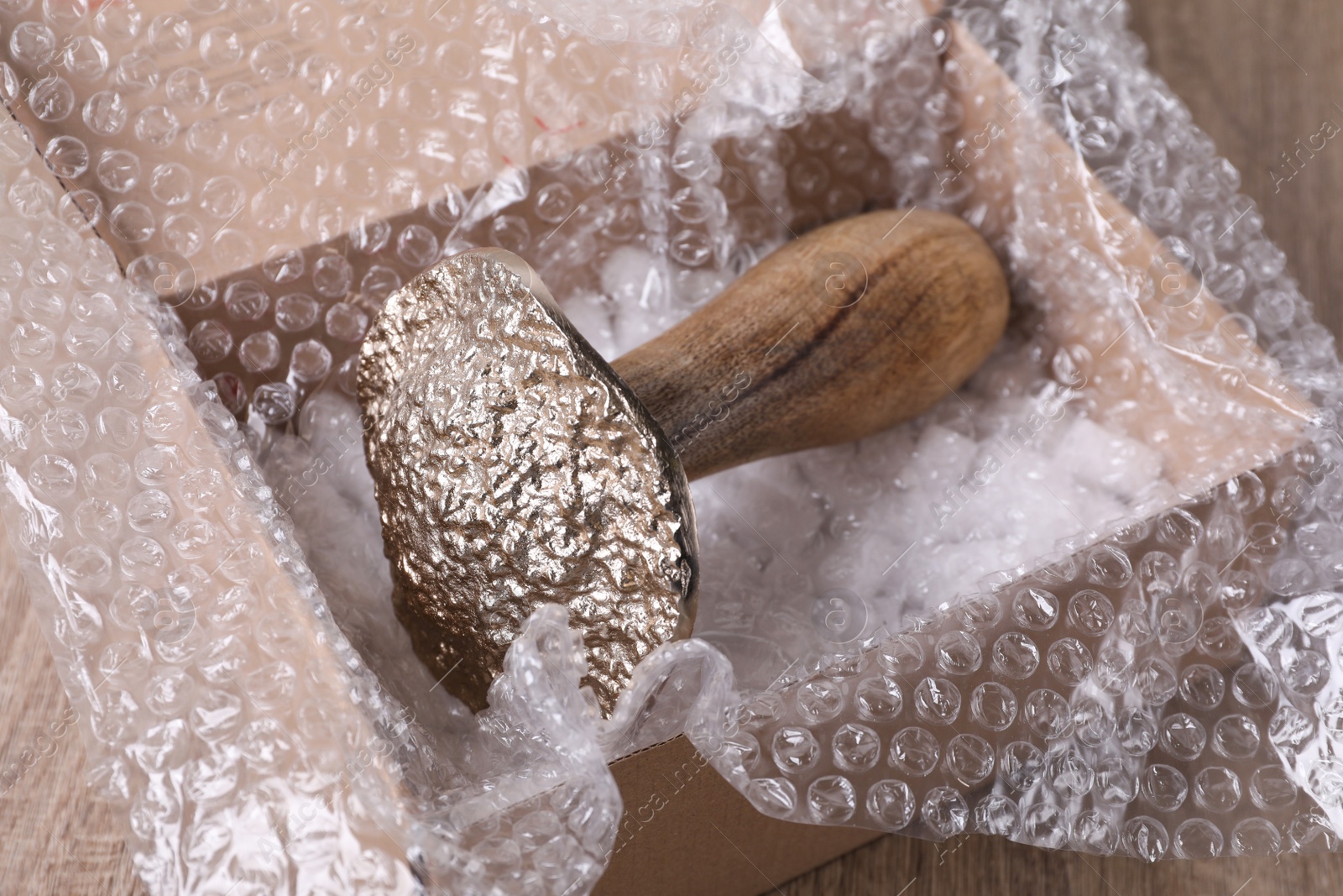 Photo of Decorative mushroom with bubble wrap and packaging foam in cardboard box on wooden table, closeup