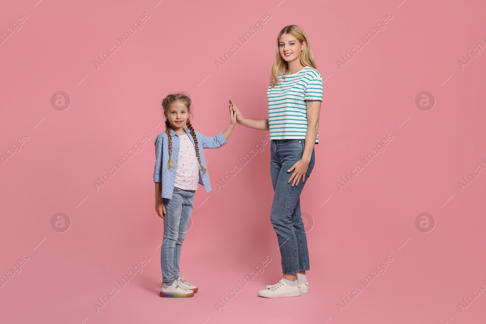 Photo of Mother and daughter giving high five on pink background