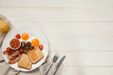 Plate of fried eggs, mushrooms, beans, bacon, tomatoes and toasts on white wooden table, flat lay with space for text. Traditional English breakfast