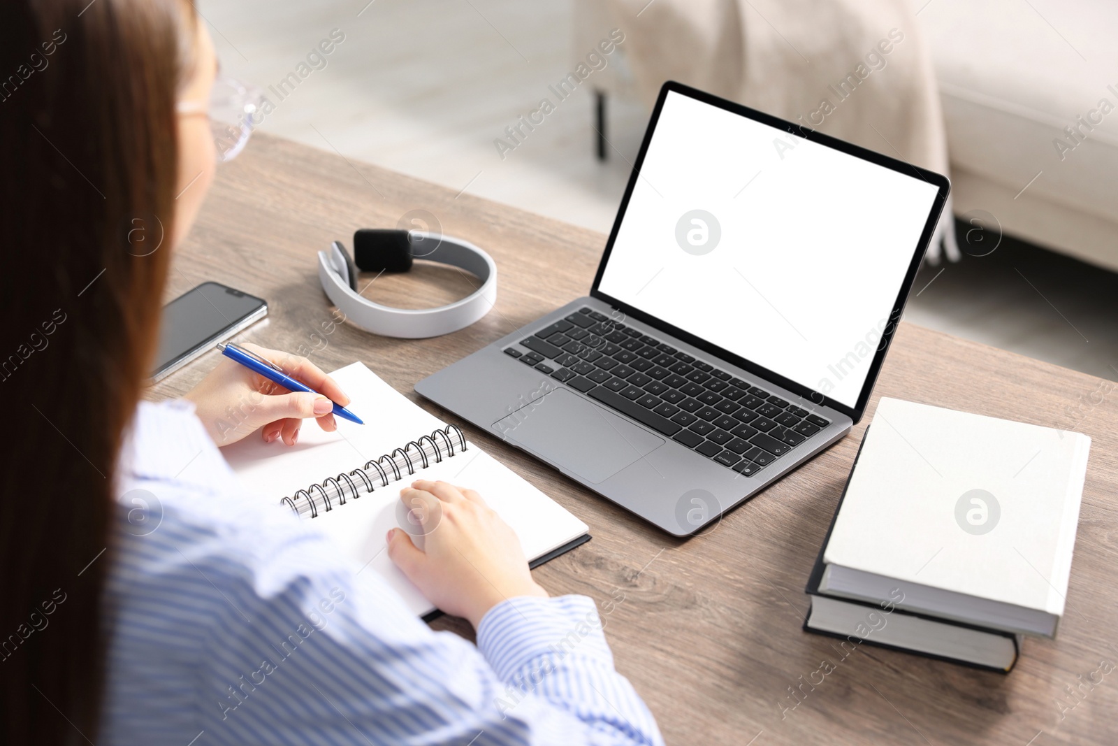 Photo of E-learning. Woman taking notes during online lesson at table indoors, closeup