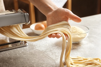 Young woman preparing noodles with pasta maker at table