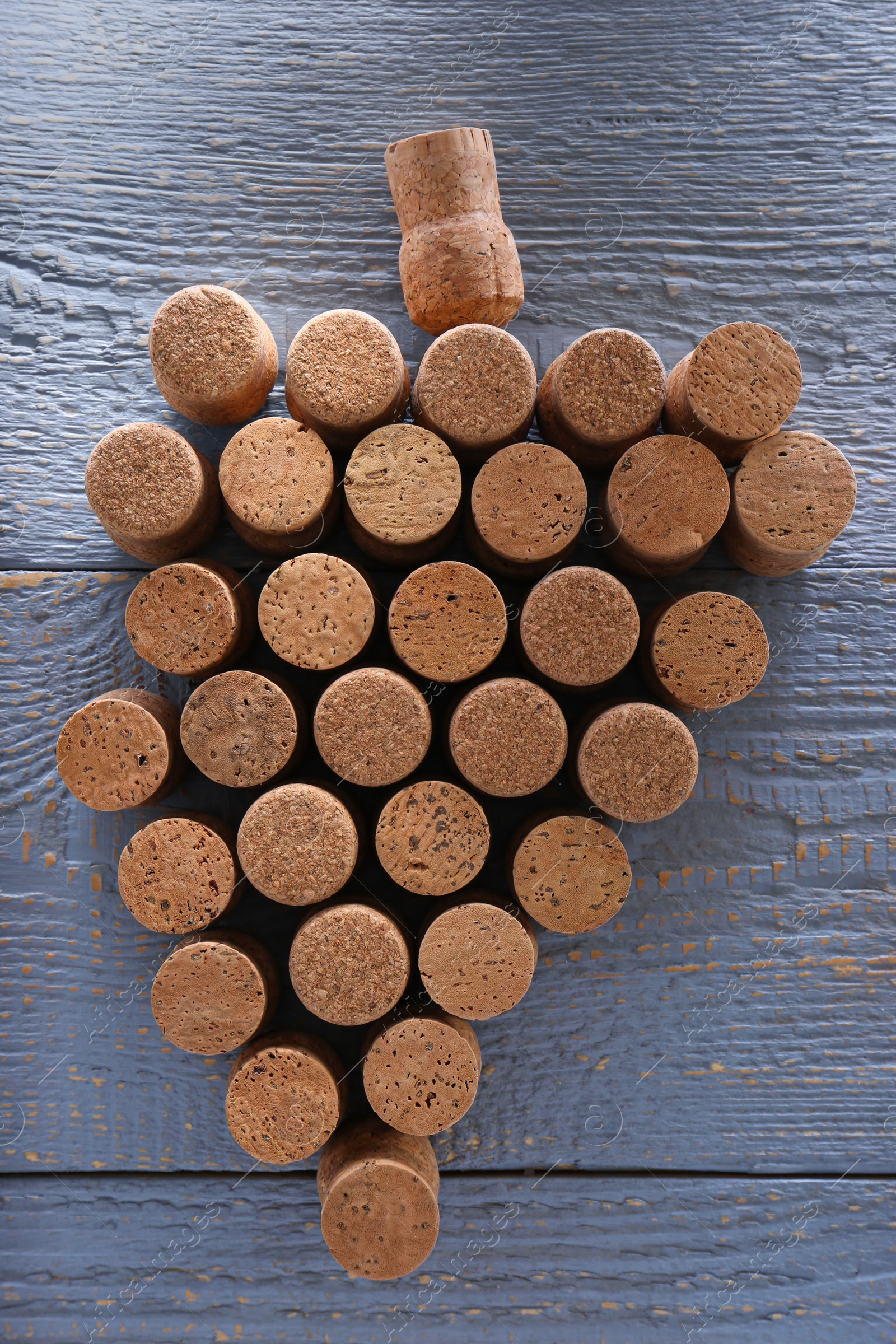 Photo of Grape made of wine bottle corks on grey wooden table, top view