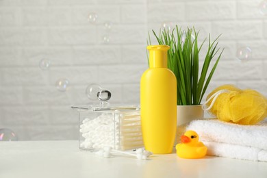 Baby cosmetic product, bath duck, cotton swabs and towel on white table against soap bubbles. Space for text