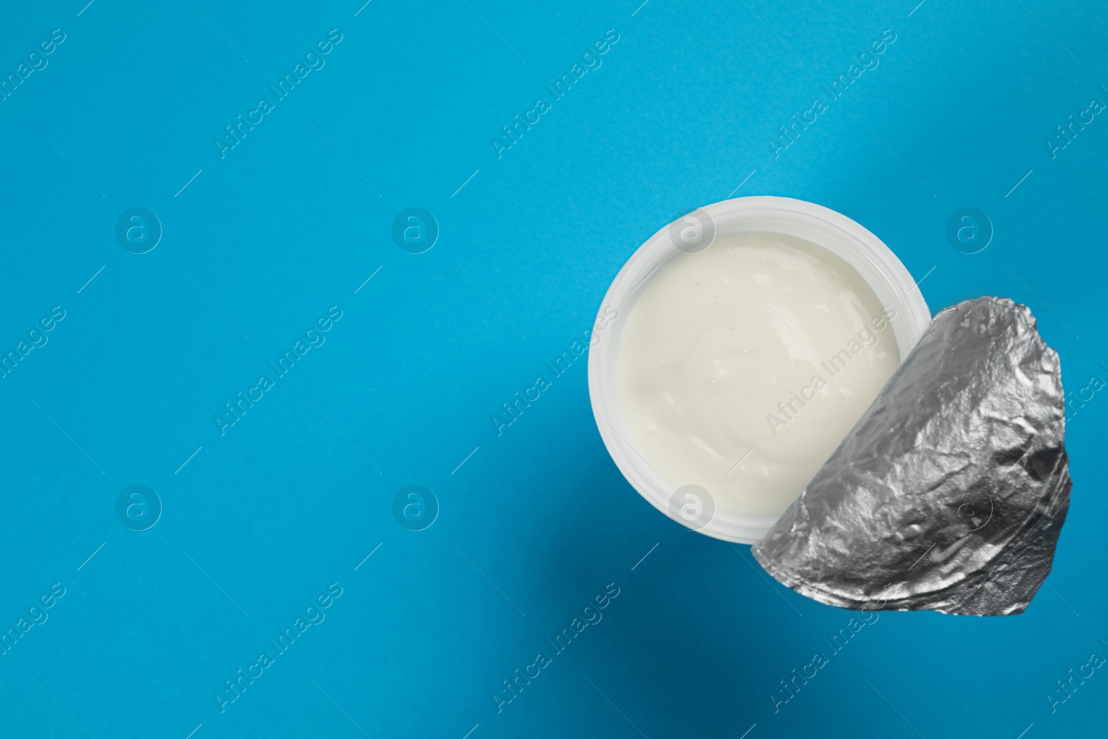 Photo of Plastic cup with tasty yogurt on light blue background, top view. Space for text