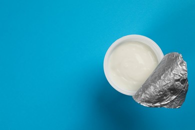 Plastic cup with tasty yogurt on light blue background, top view. Space for text