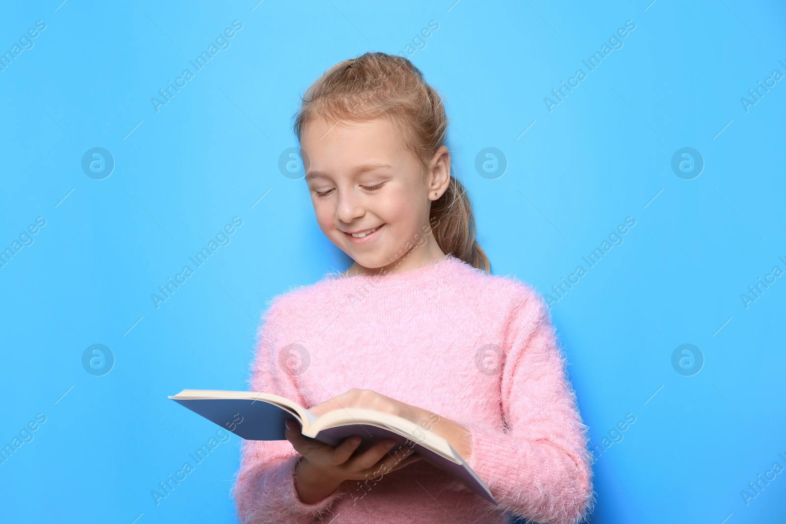 Photo of Happy little girl reading book on light blue background