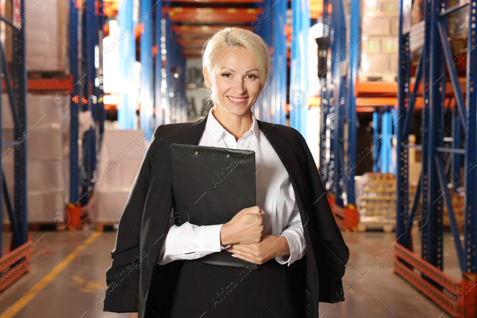 Photo of Happy manager holding clipboard in warehouse with lots of products