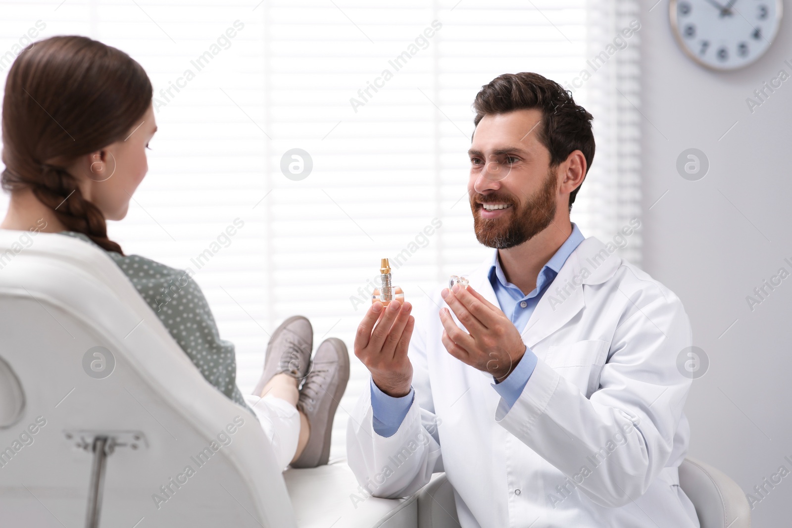 Photo of Doctor with educational model of dental implant consulting patient in clinic