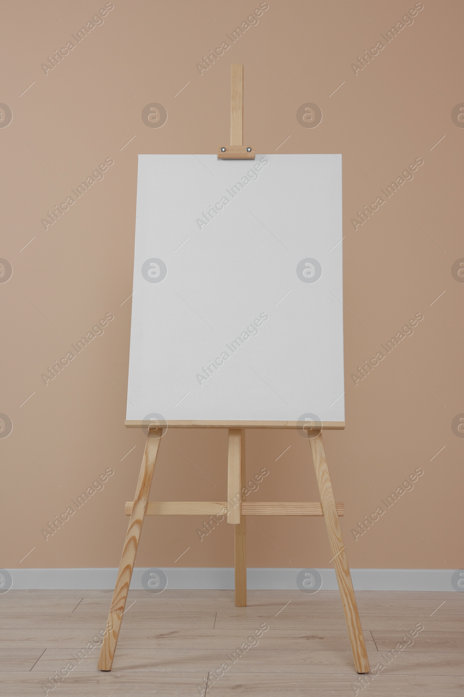 Photo of Wooden easel with blank canvas near beige wall indoors