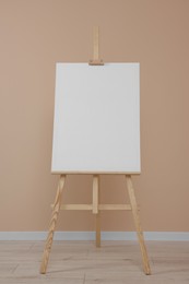 Wooden easel with blank canvas near beige wall indoors