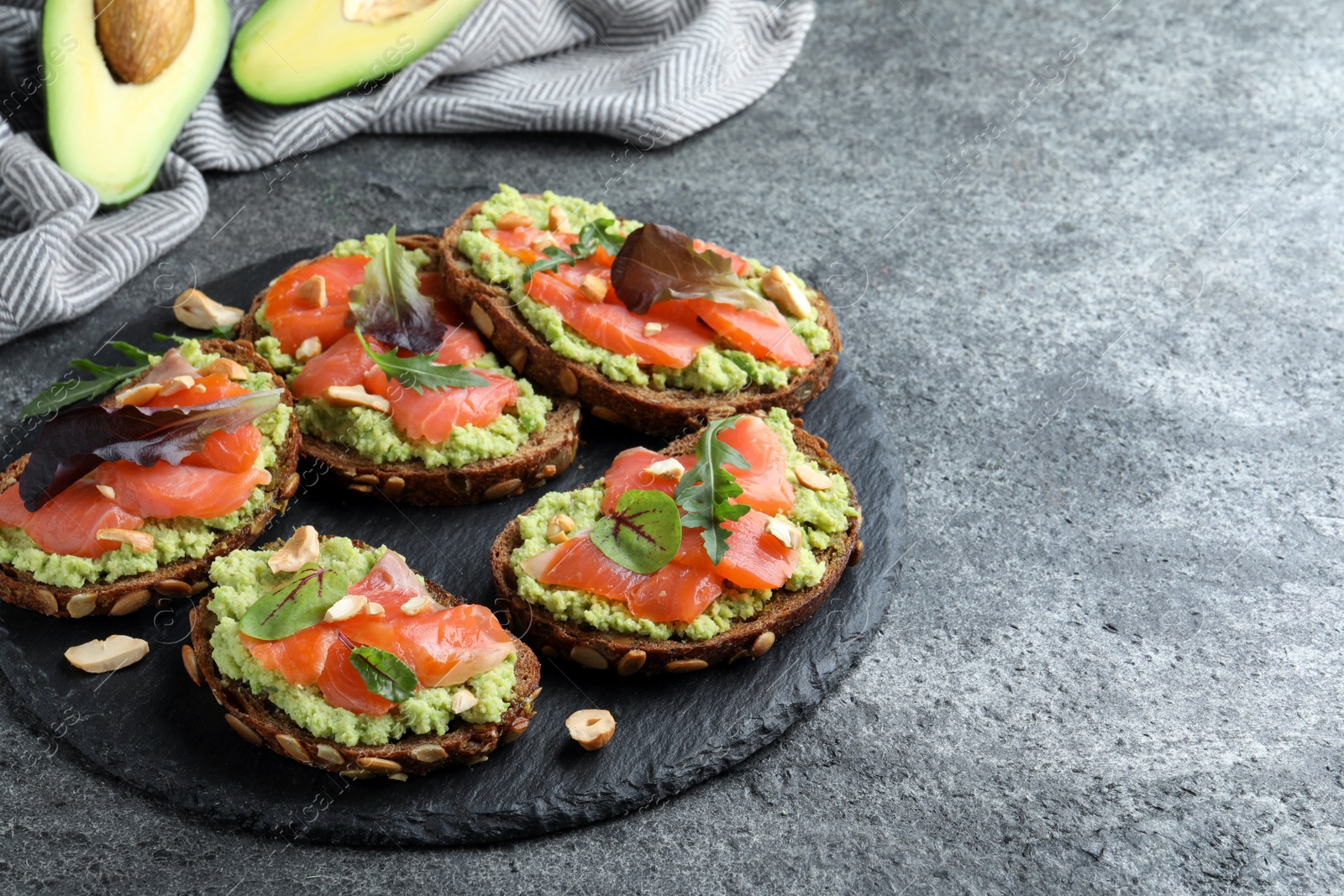 Photo of Delicious sandwiches with salmon, avocado and herbs on grey table. Space for text