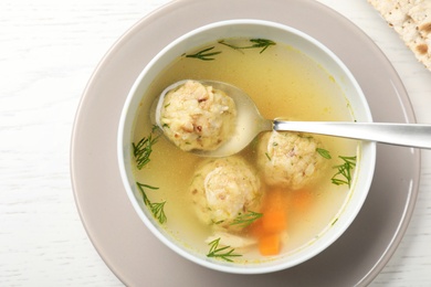 Photo of Bowl of Jewish matzoh balls soup on white wooden table, top view