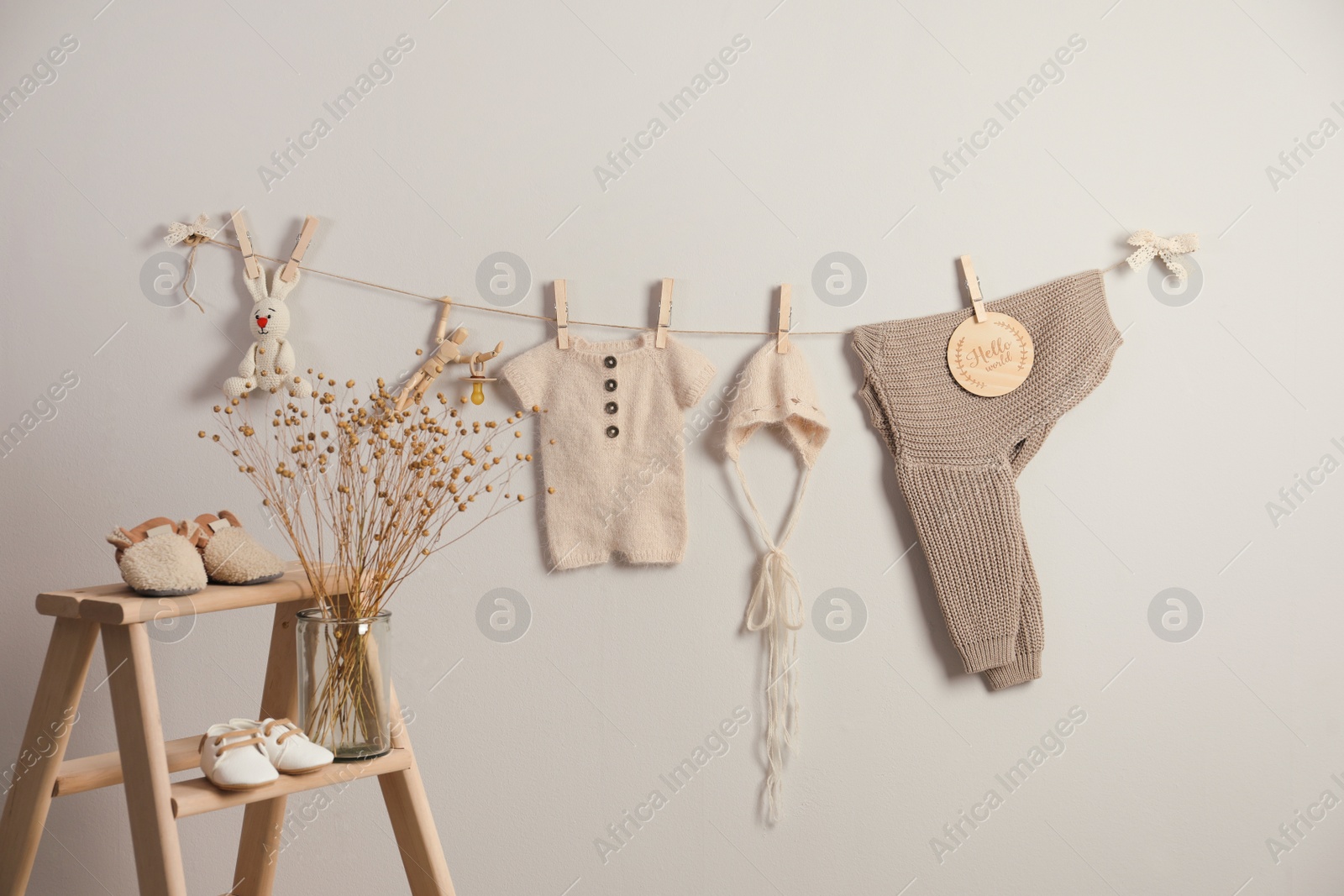 Photo of Baby clothes and accessories hanging on washing line near light grey wall