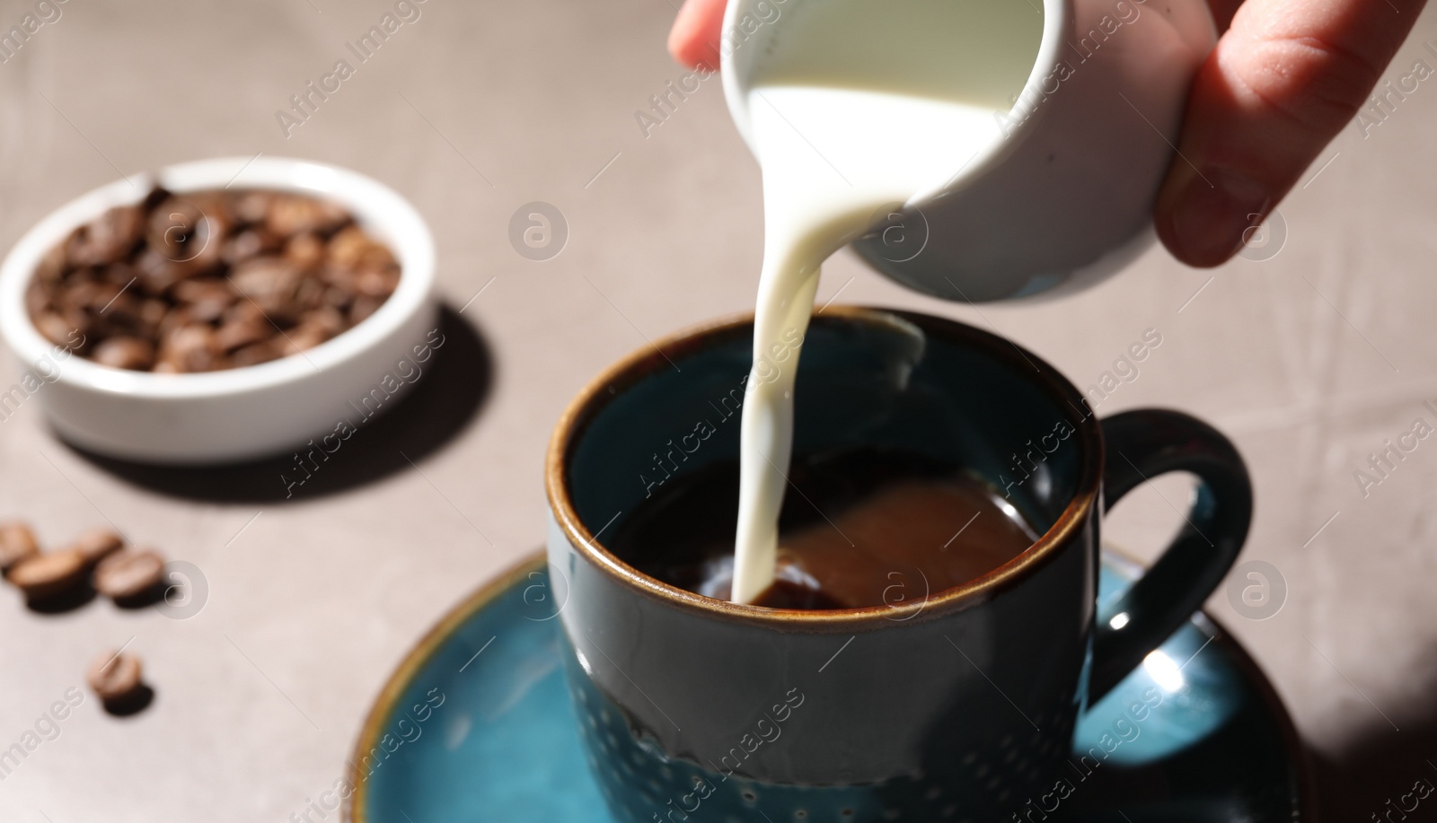 Photo of Woman pouring milk into cup with aromatic coffee at light table, closeup