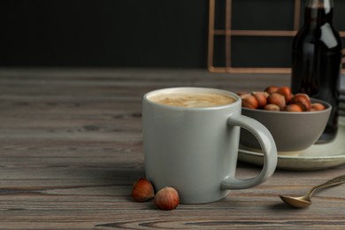 Photo of Mug of delicious coffee with hazelnut syrup on wooden table, space for text