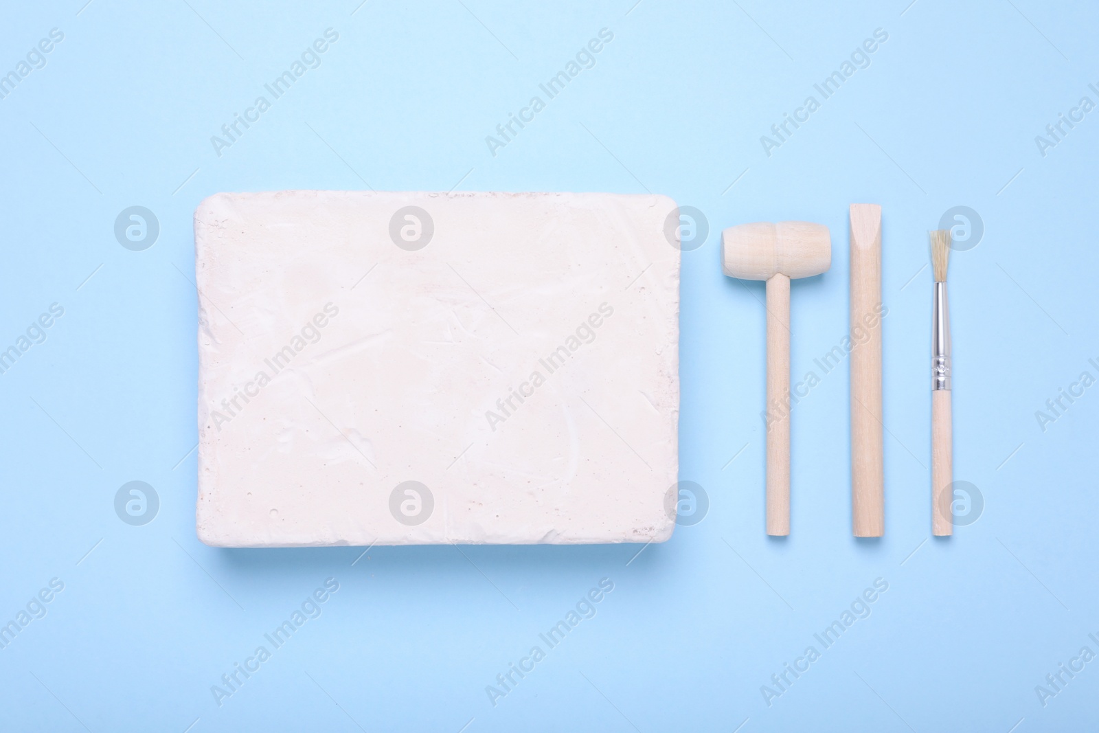 Photo of Educational toy for motor skills development. Excavation kit (plaster, digging tools and brush) on light blue background, flat lay