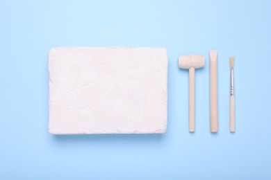 Photo of Educational toy for motor skills development. Excavation kit (plaster, digging tools and brush) on light blue background, flat lay