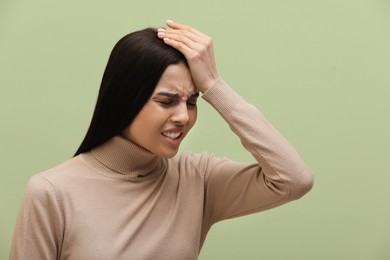 Woman suffering from migraine on light green background