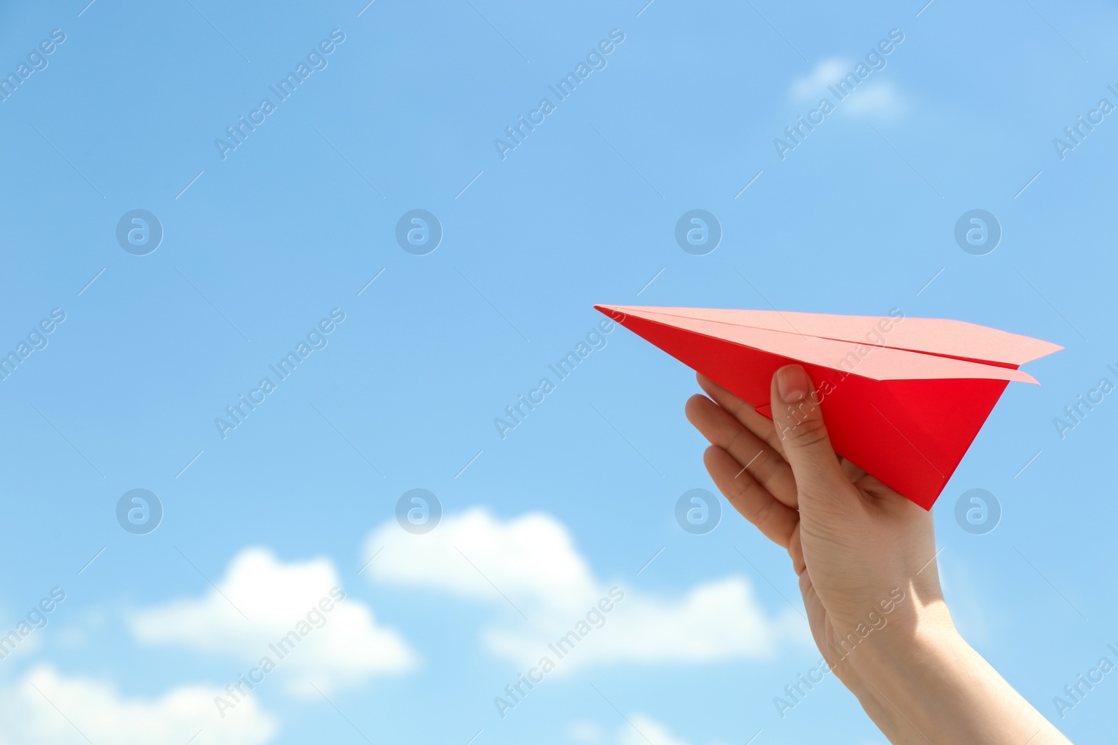 Photo of Woman holding paper plane against blue sky, closeup. Space for text