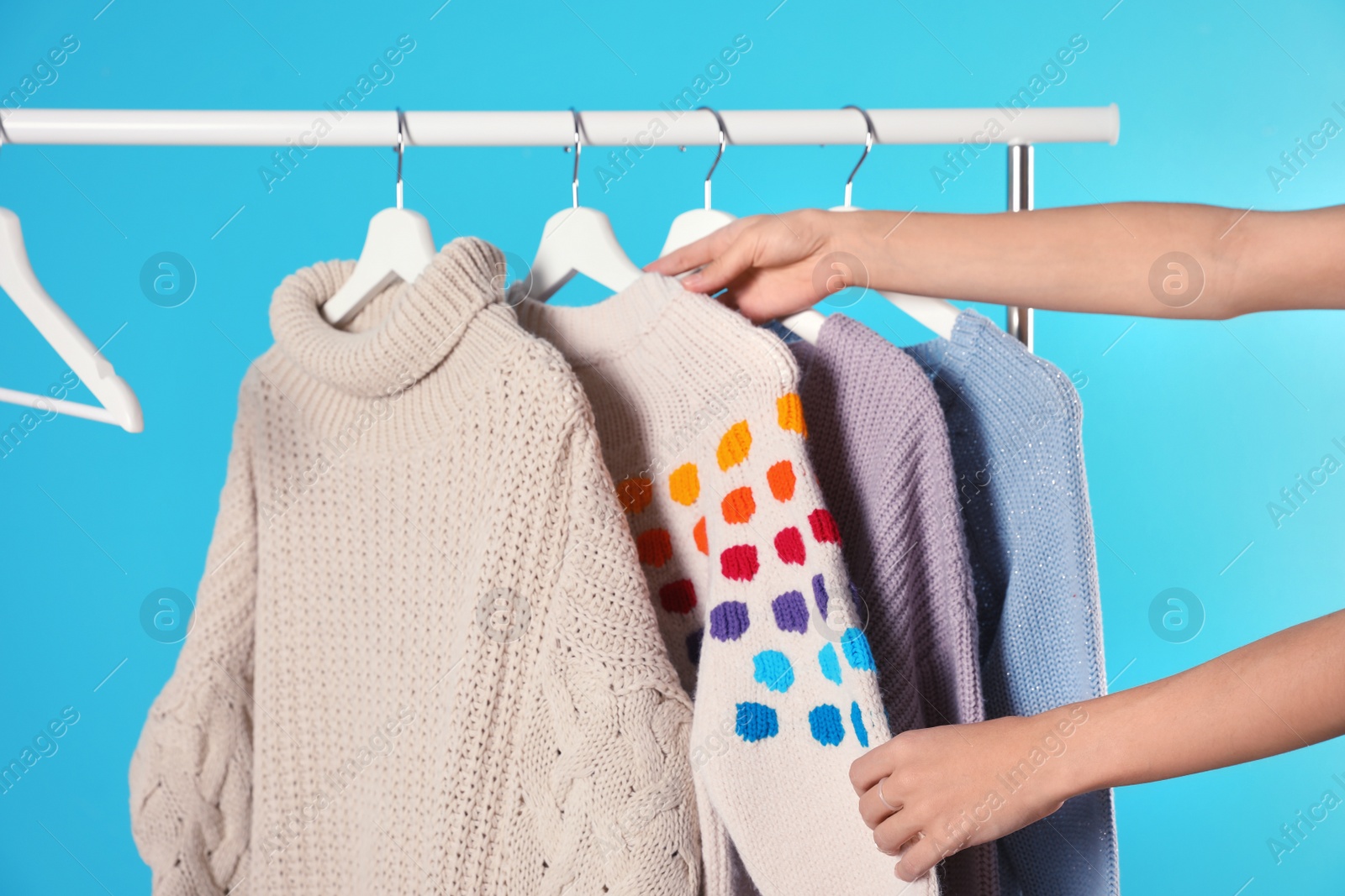 Photo of Woman choosing sweater on rack against color background