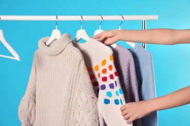 Woman choosing sweater on rack against color background