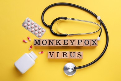 Words Monkeypox Virus made of wooden cubes, pills and stethoscope on yellow background, flat lay