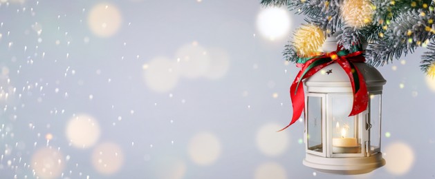 Christmas lantern with candle hanging on snowy fir tree branch against light background, space for text. Banner design