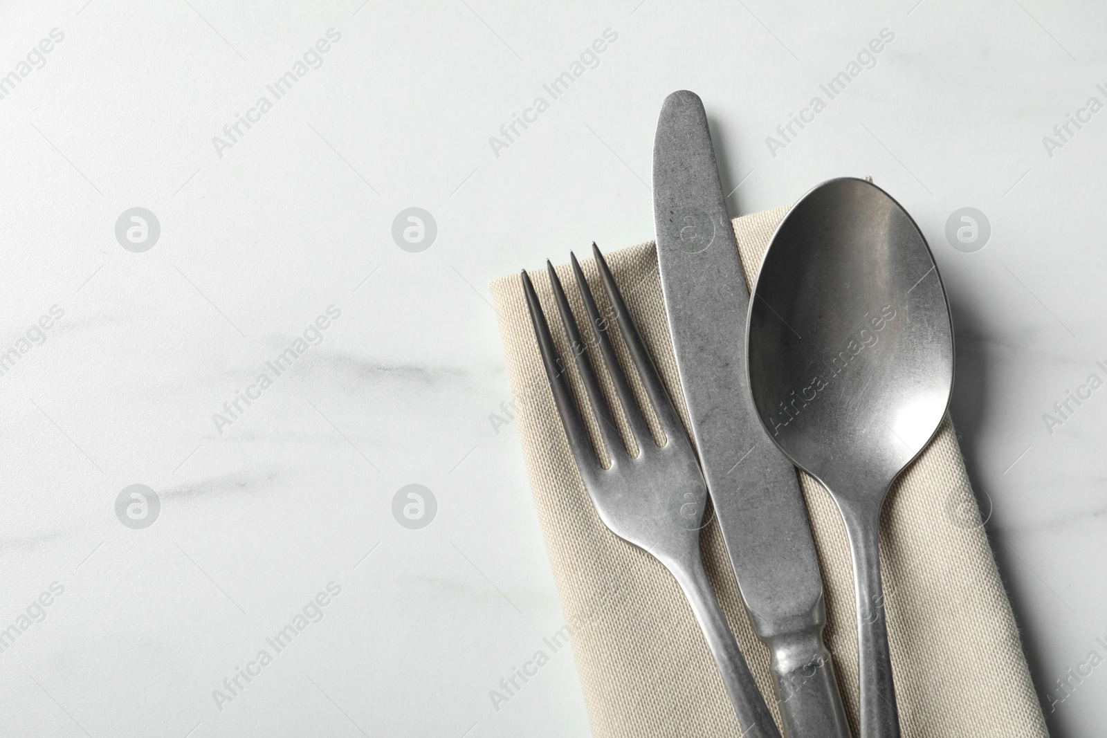 Photo of Set of stylish cutlery and napkin on white marble table, top view. Space for text