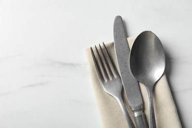 Photo of Set of stylish cutlery and napkin on white marble table, top view. Space for text